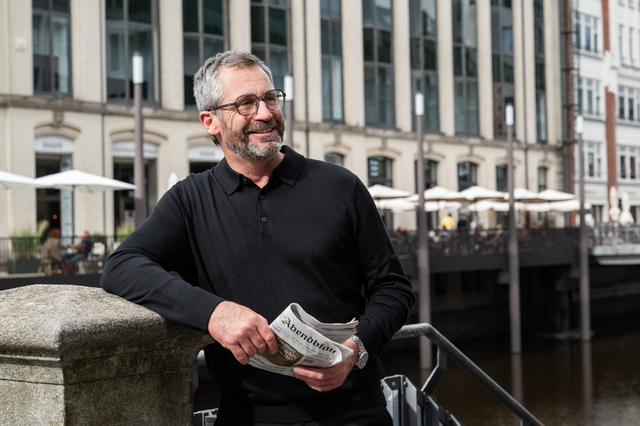 man, zwarte polo, bril, krant, stadsomgeving