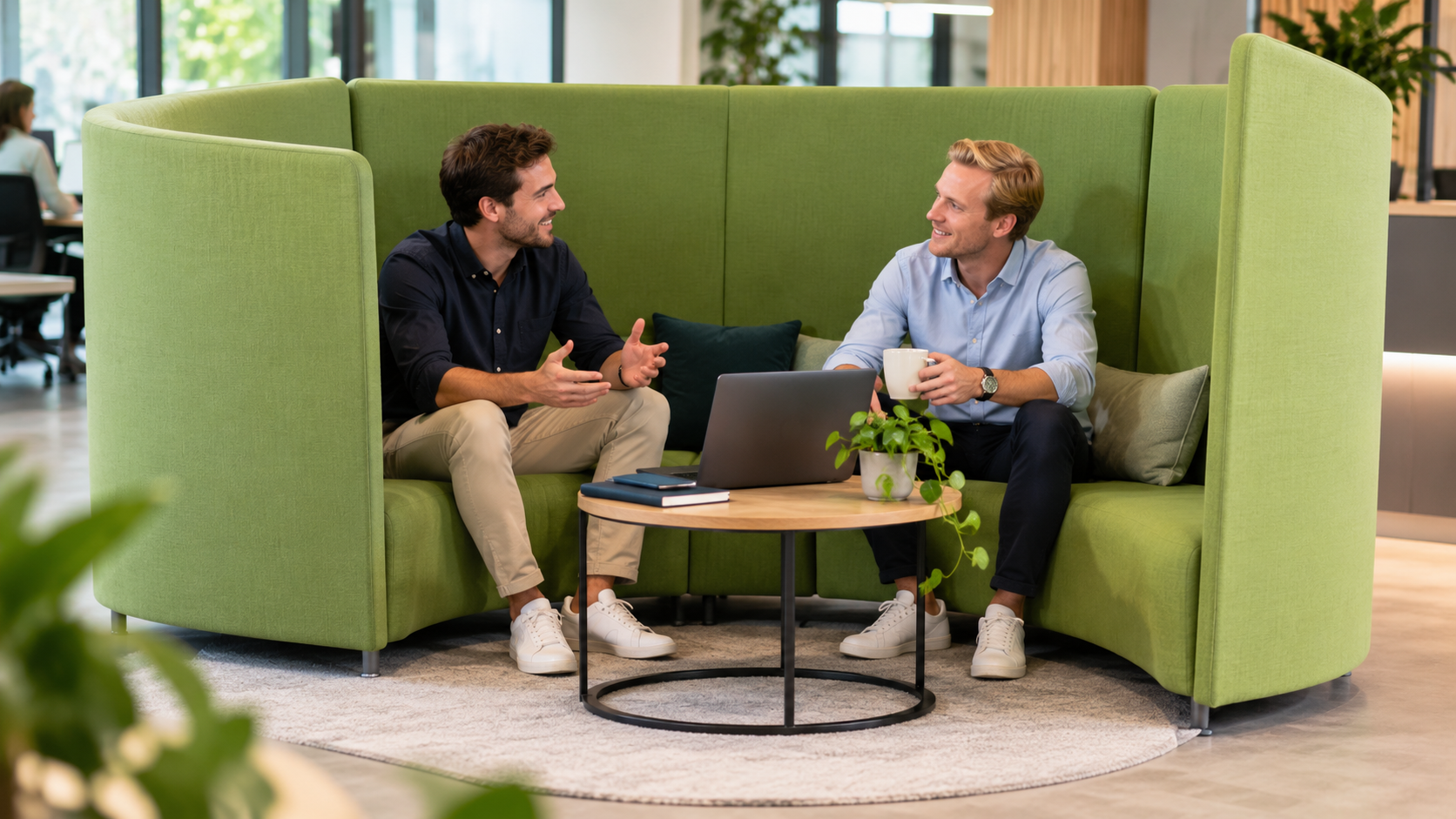 Twee mannelijke collega’s overleggen in een groene halfronde akoestische bank in een moderne kantooromgeving.