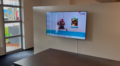 Digitaal informatiescherm aan de wand van een vergaderruimte voor presentaties, videobeelden en zakelijke communicatie.