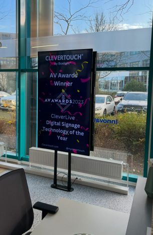 Vrijstaand verticaal Clevertouch informatiescherm op slanke poten voor digitale communicatie en presentaties in een zakelijke omgeving.