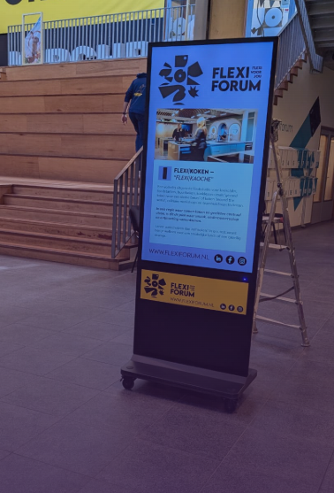 Mobiele digitale informatiezuil op wielen met een verticaal scherm voor bezoekersinformatie en evenementencommunicatie.