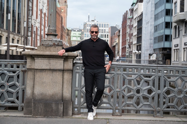 man, zwart polo, zwart pantalon, witte sneakers, stedelijke brug railing