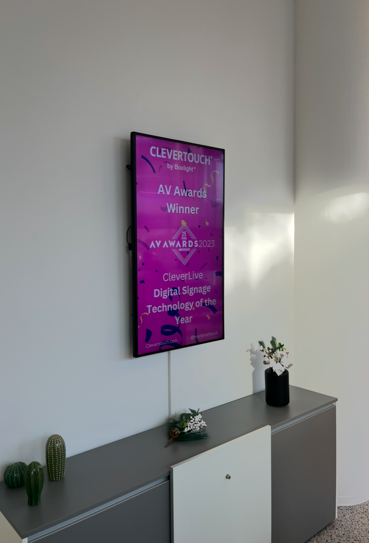 Verticaal gemonteerd digitaal informatiescherm voor narrowcasting en professionele communicatie in een kantooromgeving.